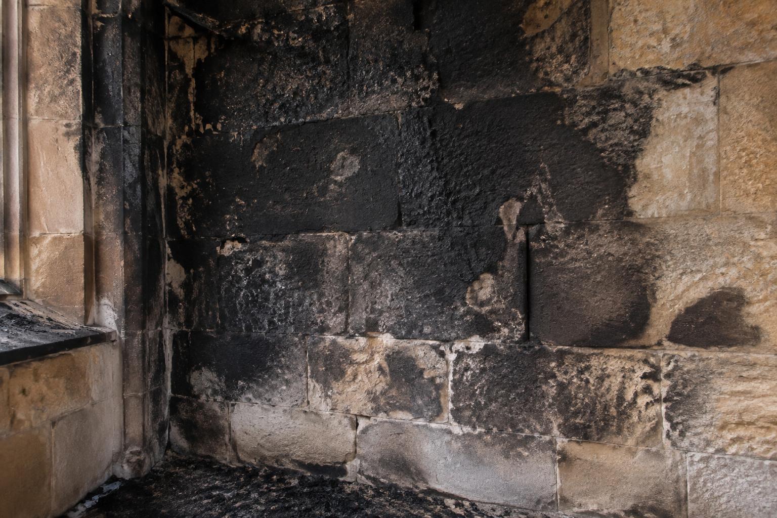 Sandstone wall heavily blackened by soot and smoke staining after a fire.