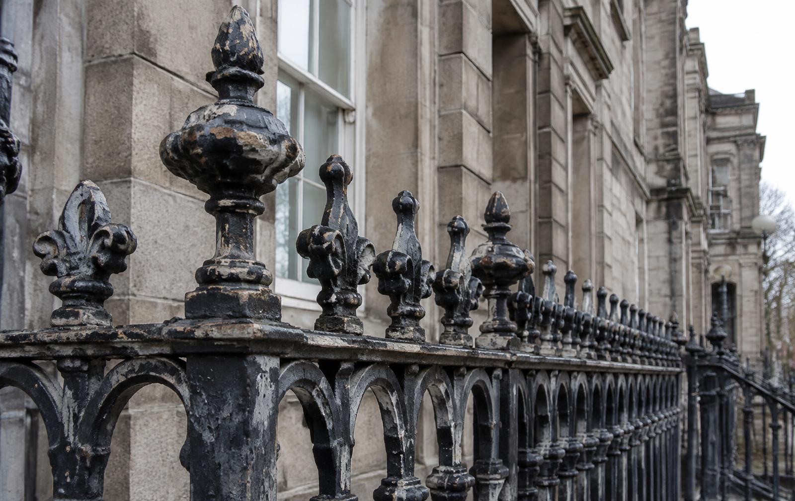 Historic cast iron railings with layered flaking paint in front of a granite building