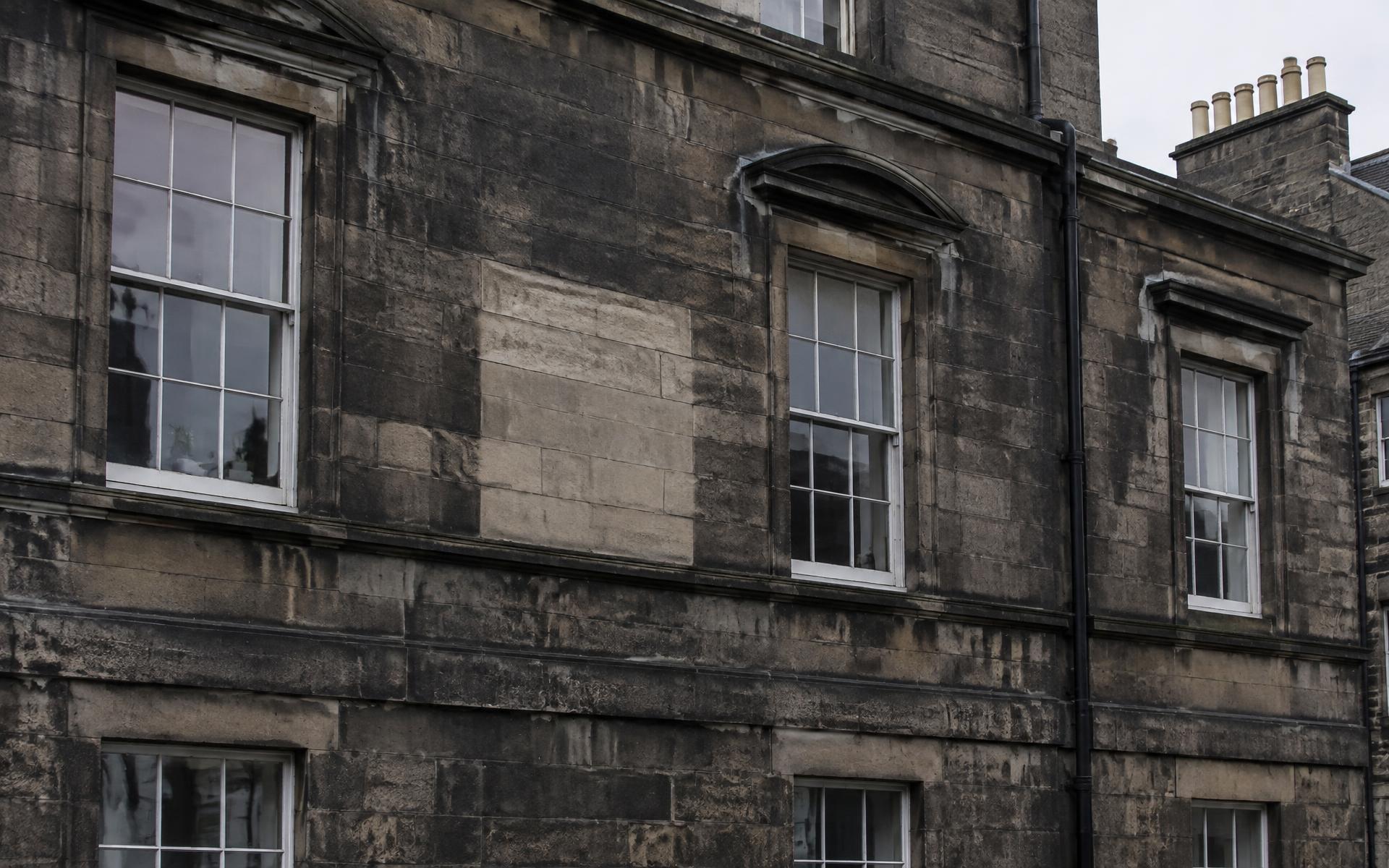 Soot-darkened granite building elevation with a cleaner test area of stonework
